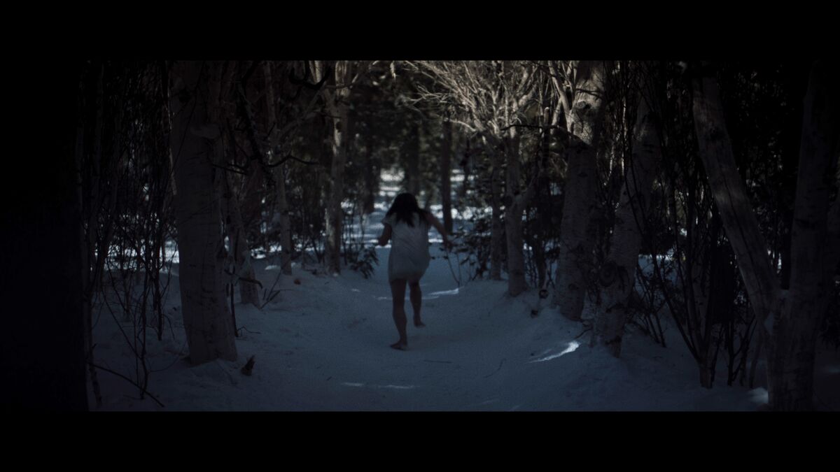 A girl runs through the woods in a dark scene from "Yellowjackets."