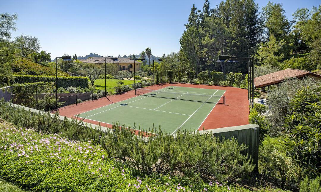 The tennis court is surrounded by foliage.