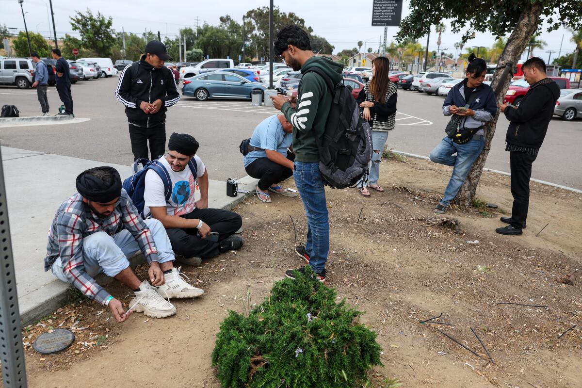 Migrants check their phones at a parking lot.
