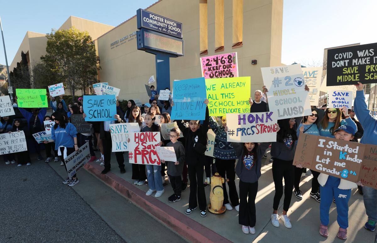Adults and children hold up signs on a sidewalk.
