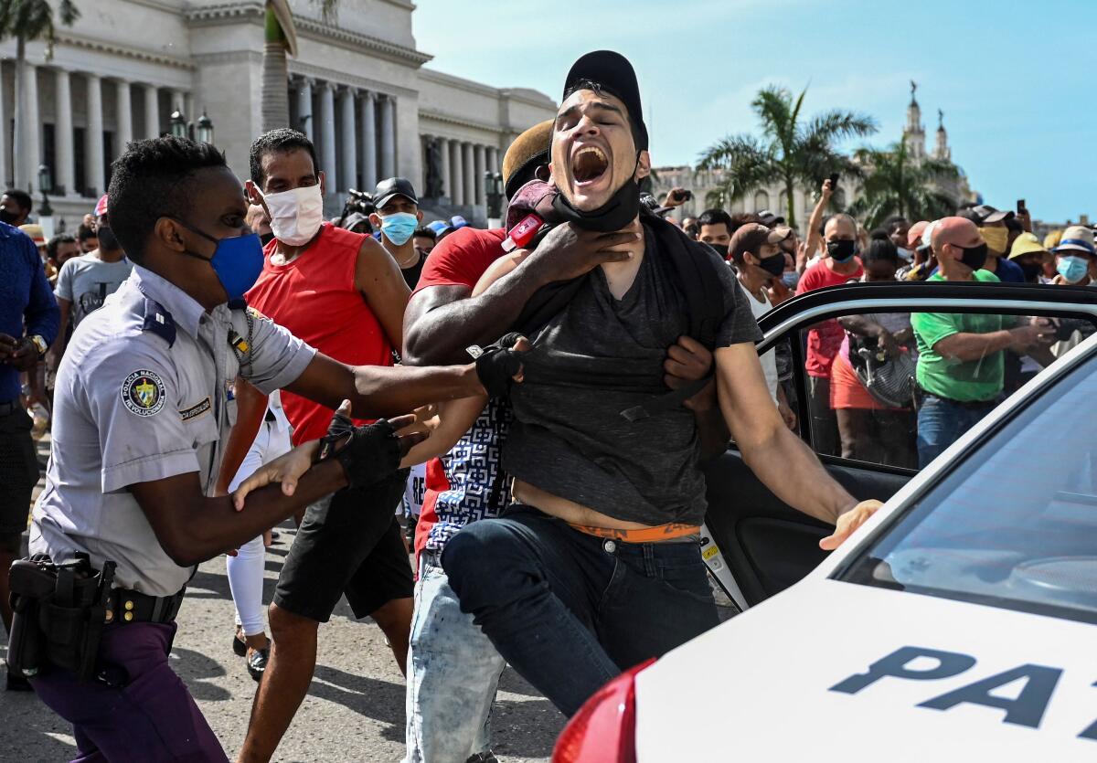 A man who is yelling is arrested by two officers who have their hands on his arm, body and neck. 