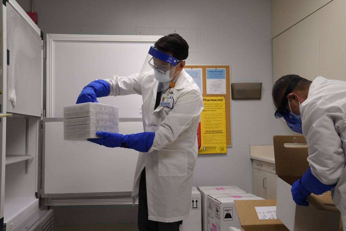 A man in a lab coat places trays of COVID-19 vaccine into a freezer at Kaiser Permanente Los Angeles Medical Center