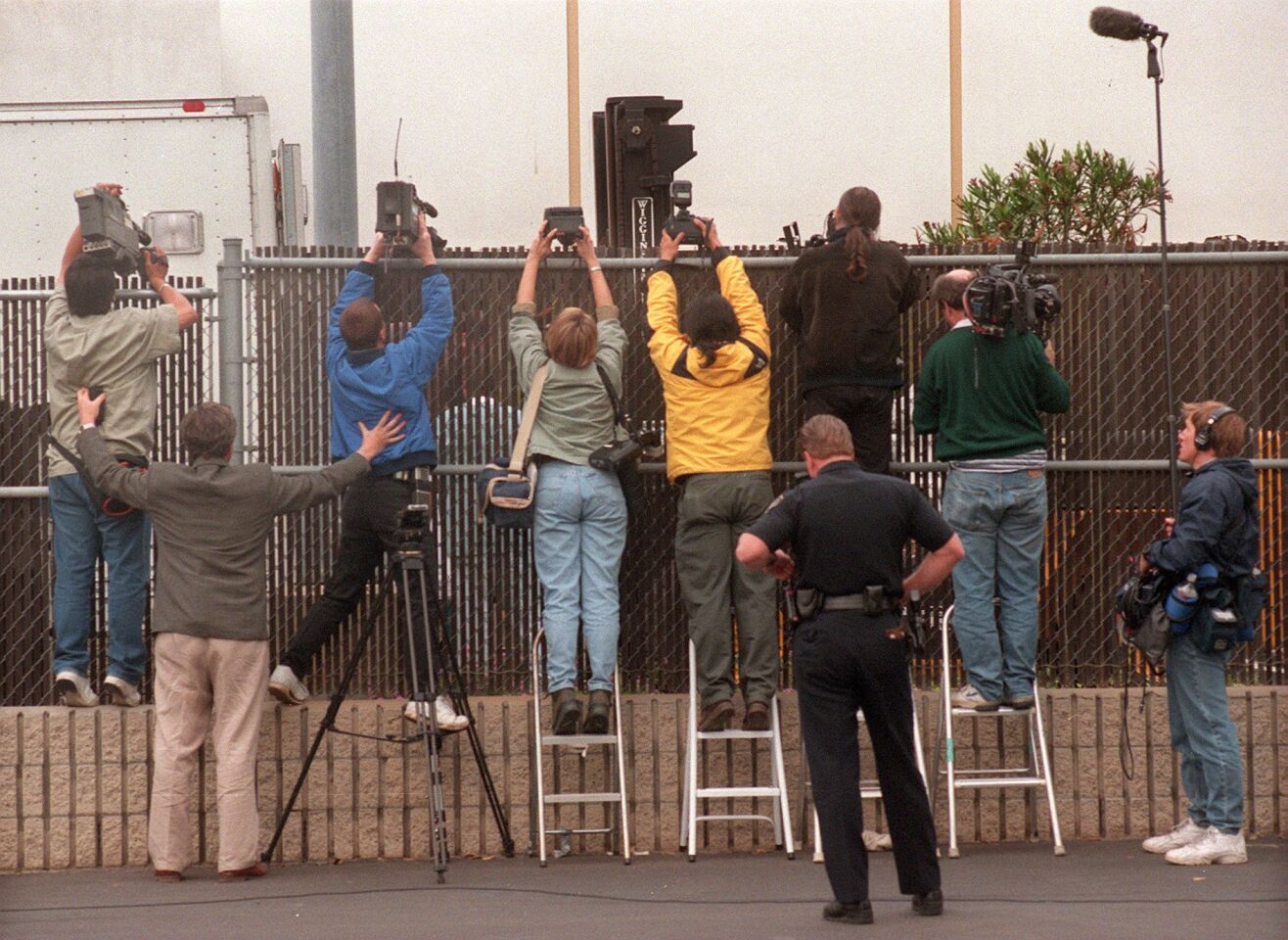 Photographers did what they could to get their cameras over a chain link fence to shoot photos of bodies being unloaded at the Medical Examiner's Office in Kearny Mesa on March 27, 1997. The day before the Heaven's Gate mass suicide was discovered inside a Rancho Santa Fe mansion.
