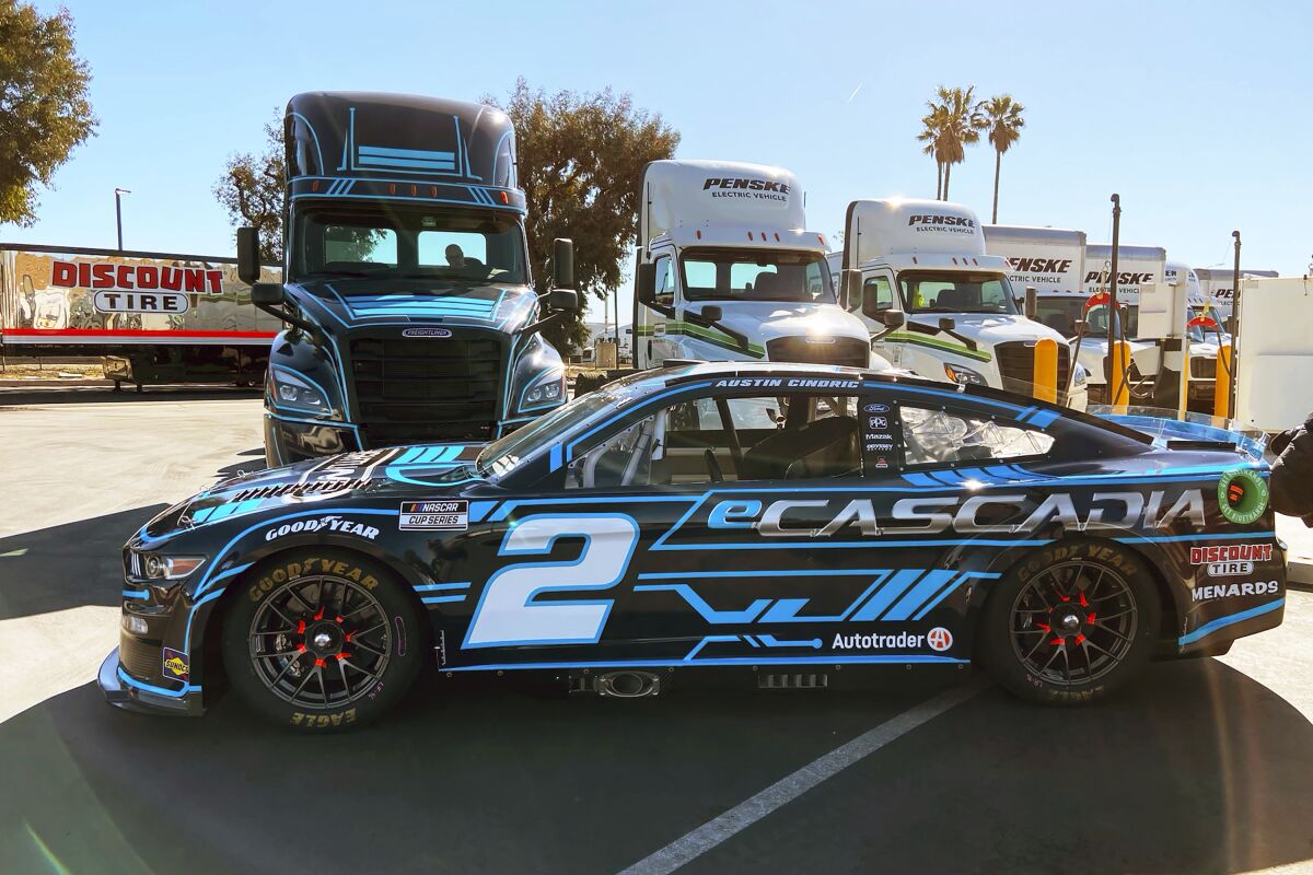 The No. 2 Ford that will be driven by Austin Cindric at the Los Angeles Coliseum this week sits in front of the Team Penske fully electric Freightliner eCascadia hauler, with the same paint scheme, at Penske Truck and Leasing in Ontario, Calif., Thursday, Feb. 3, 2022. (AP Photo/Jenna Fryer)