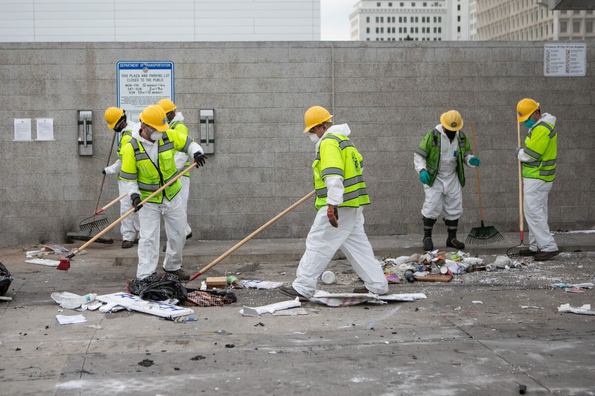 City workers in white outfits and yellow helmets clear Toriumi Plaza with rakes and brooms