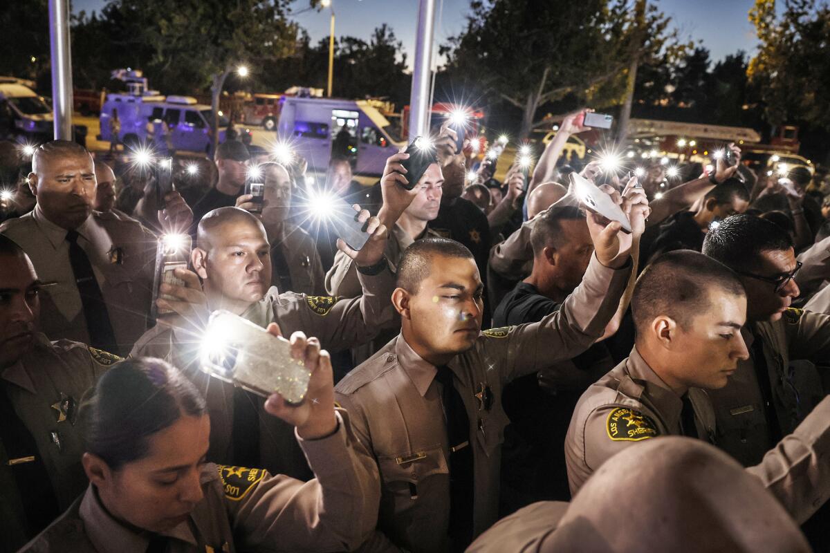 Sheriff's deputies hold up their lighted phones at a vigil.