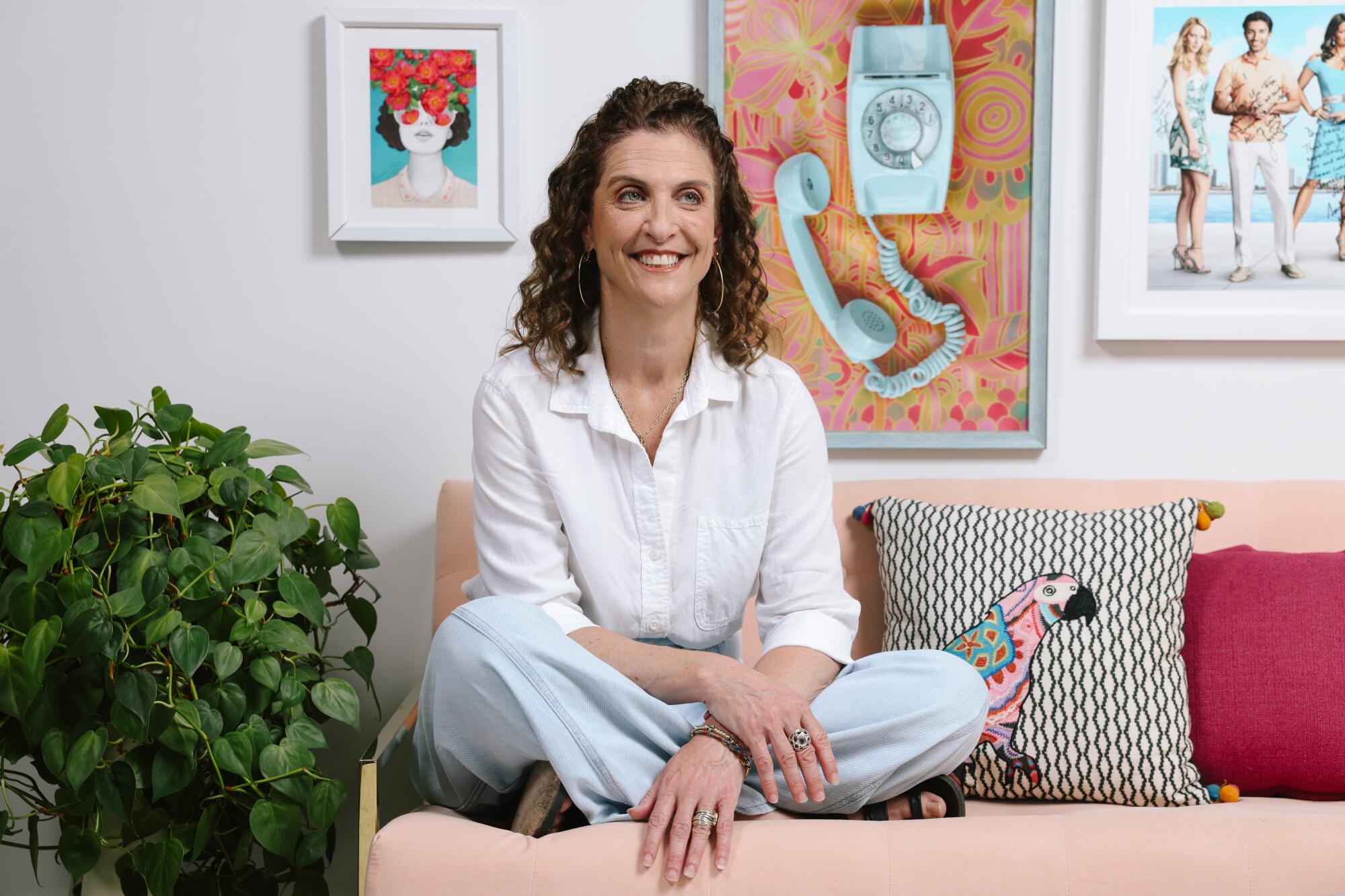 A woman with curly hair sits cross-legged on a couch