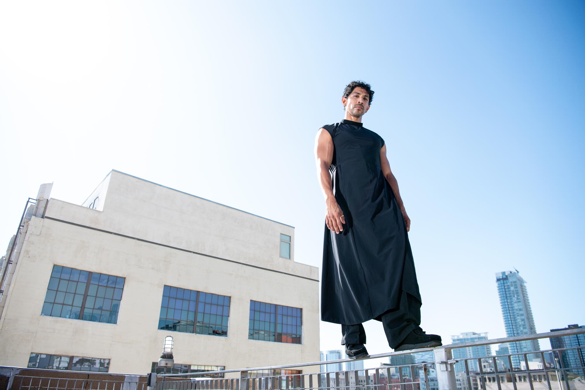 A man wearing a long black tunic stands on a building rail.