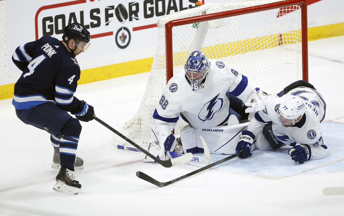 Tampa Bay Lightning's Victor Hedman (77) collides with goaltender Andrei Vasilevskiy (88) as he saves the shot from Winnipeg Jets' Neal Pionk (4) during the third period of an NHL hockey game Tuesday, March 8, 2022 in Winnipeg, Manitoba.(Fred Greenslade/The Canadian Press via AP)