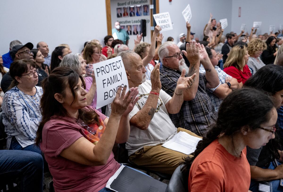 A woman holds a sign as people around her applaud during a meeting in Murrieta. 