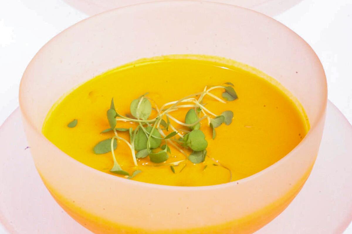 A frosted glass bowl half-filled with orange soup topped with watercress