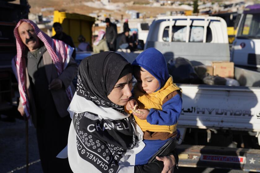 A Syrian refugee woman carries her child as she prepares to go back home to Syria as part of a voluntary return, in the eastern Lebanese border town of Arsal, Tuesday, May 14, 2024. Hundreds of Syrians refugees left a remote northeastern Lebanese town back to Syria in a convoy, amid a surge in anti-refugee sentiment in the small, crisis-hit country. Lebanese officials for years has urged the international community to resettle the refugees in other countries or help them return to Syria. (AP Photo/Hussein Malla)