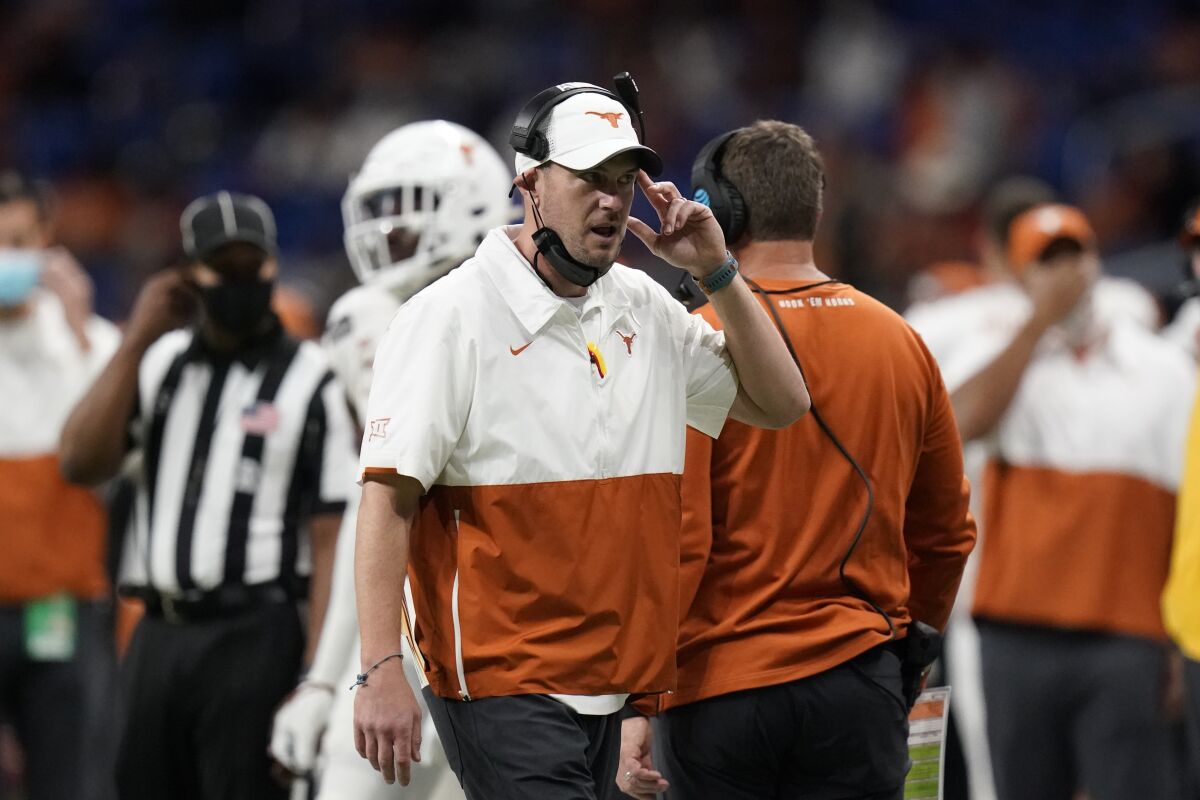 Texas head coach Tom Herman talks into a headset while players, a referee and Texas staff are behind him.