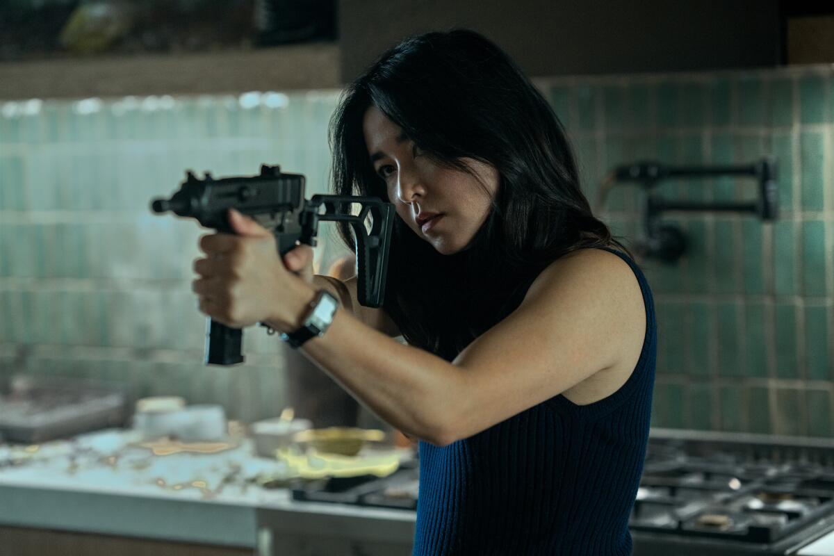 Una mujer en una cocina apunta con un arma grande a un objetivo invisible.