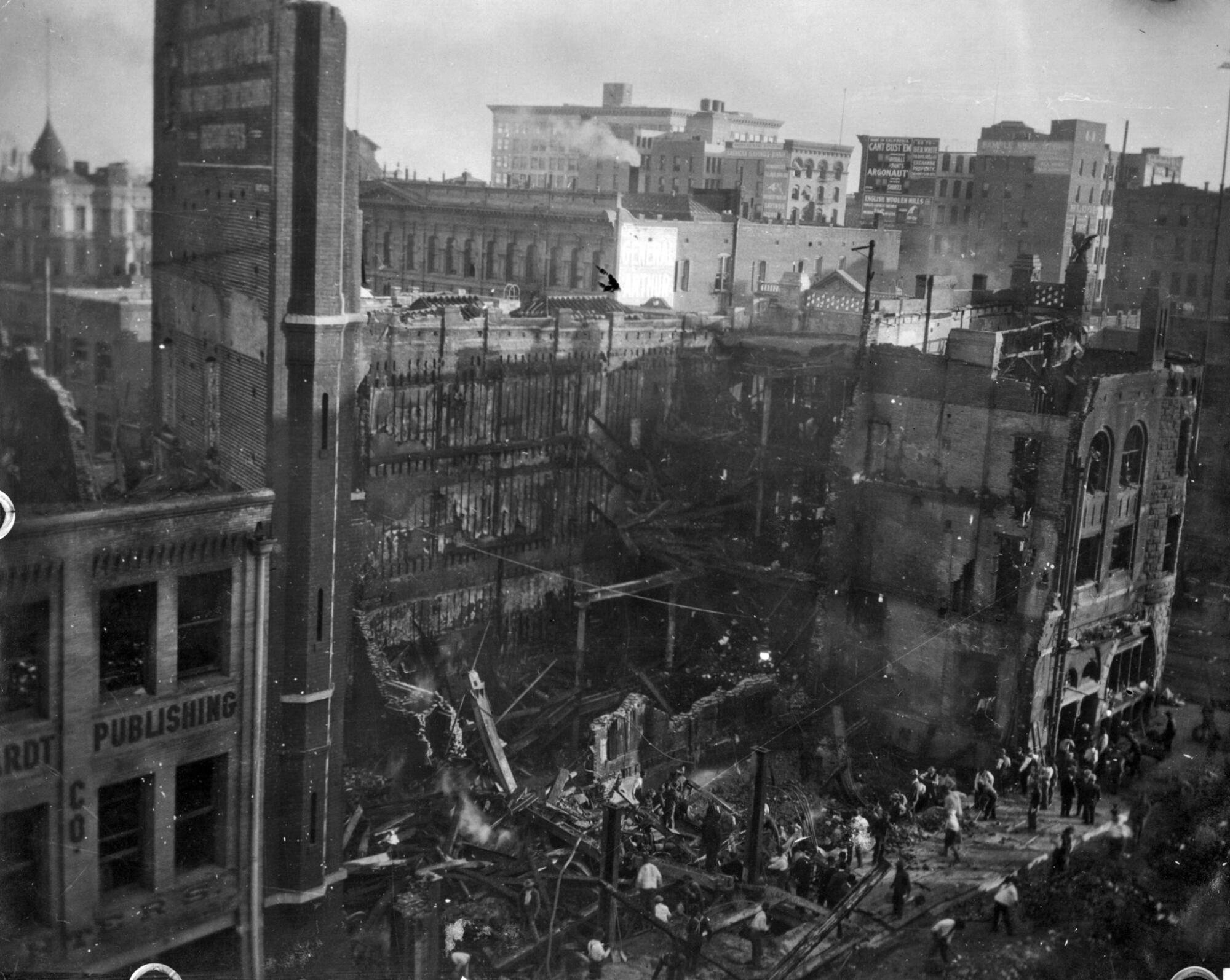A black-and-white photo of a large building, a huge section of it obliterated, and over a dozen people on the sidewalk below.