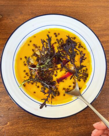 An overhead of butternut squash and carrot soup with crispy lentils. A spoon lifts a bite from the bowl at Mangette.