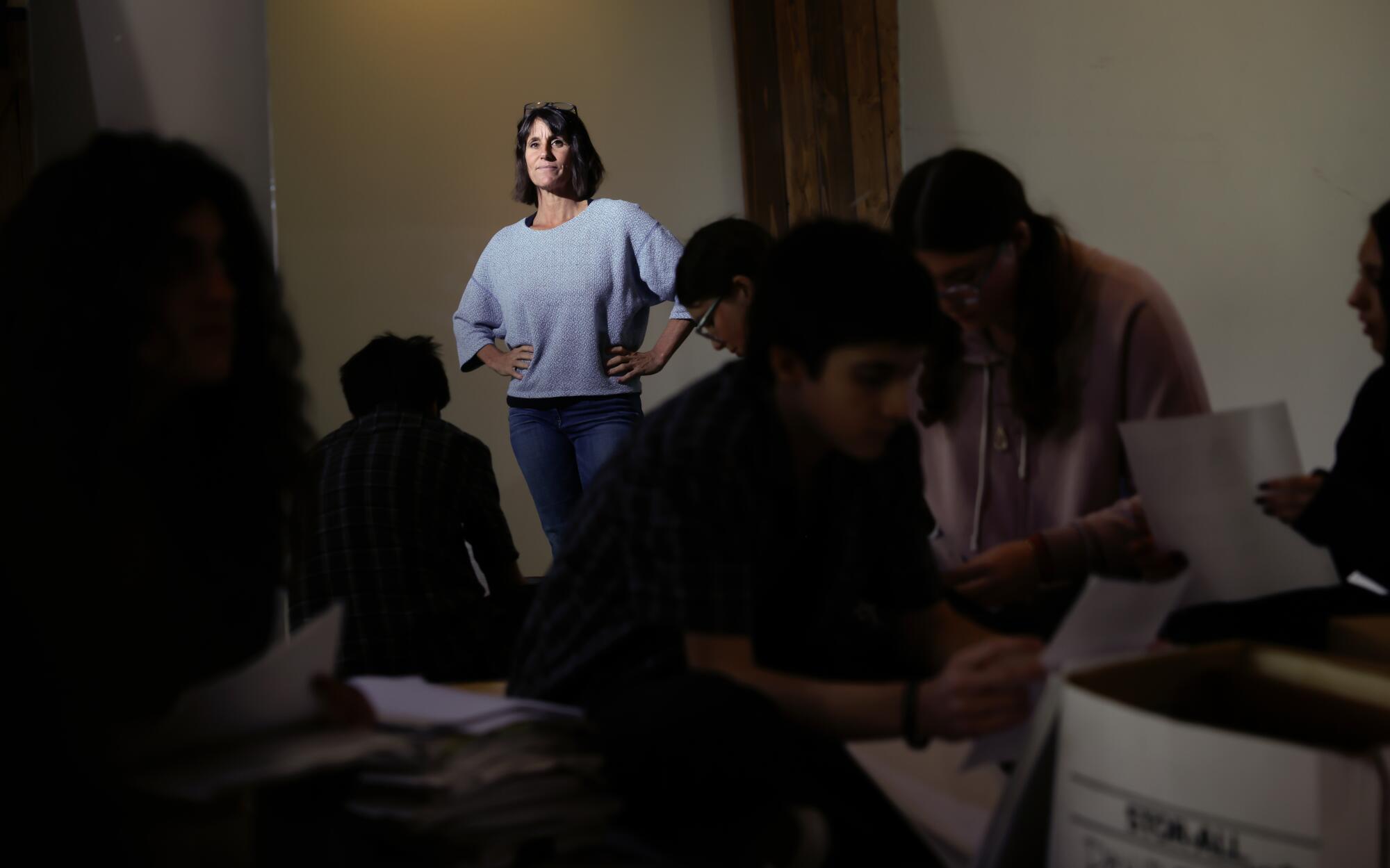 A woman stands in the back and other people hold papers in a room.