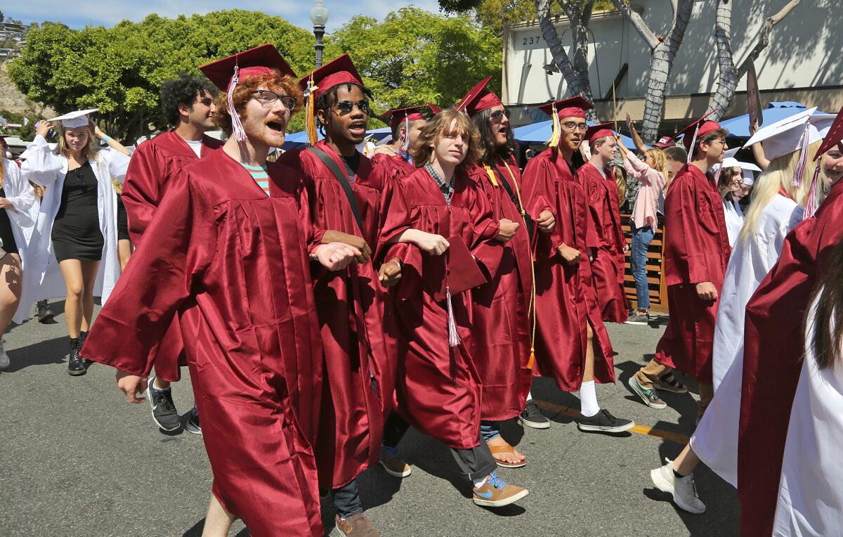 Graduates walk arm in arm as they parade down Ocean Avenue during a Laguna Beach High class of 2021 graduation event.
