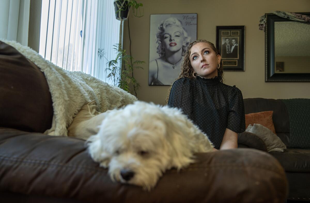 Kelsie Matthews looks up as she sits on her couch with her dog in the foreground. (Mel Melcon / Los Angeles Times)