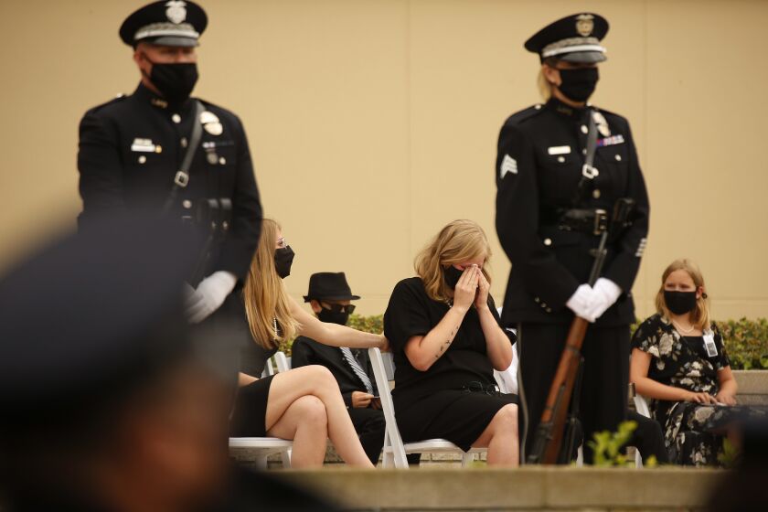 LOS ANGELES, CA - AUGUST 06: Megan Flynn, right, domestic partner of LAPD Officer Valentin Martinez who is pregnant with twins is comforted by her sister Shannon Bevers, during the funeral of Officer Martinez, the agency's first sworn employee to die of complications from the COVID-19. The social distance memory service was held at Forest Lawn Hollywood Hills' Hall of Liberty this morning. Martinez was a 13-year veteran of the department and is presumed to have contacted the virus on duty. He was 45 when he died on July 24, 2020, leaving behind his mother, Maria Martinez, his siblings and his domestic partner, Megan Flynn, who is pregnant with their twins. Los Angeles on Thursday, Aug. 6, 2020 in Los Angeles, CA. (Al Seib / Los Angeles Times)