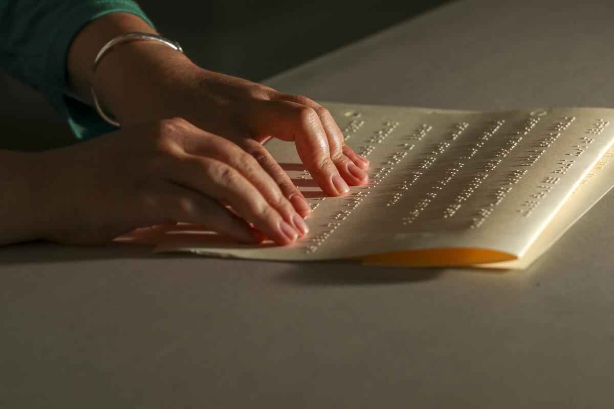 Closeup of a girl's fingers resting on Braille dots on thick yellow paper