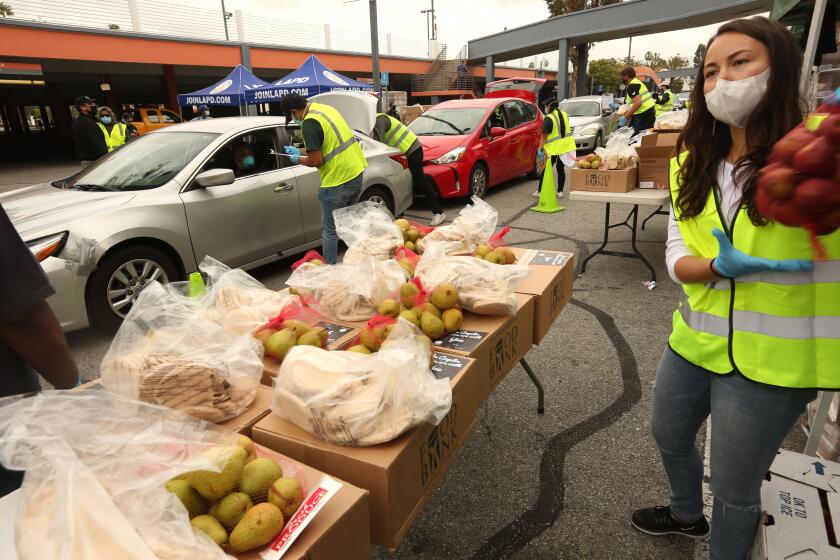 LOS ANGELES, CA - APRIL 17, 2020 - Volunteer Emi Lea Kamemoto, right, moves bags of food to a nearby table as other volunteers load up people's cars with boxes of food in the Crenshaw District on April 17, 2020. Cars lined up for blocks for the Los Angeles County Federation of Labor, in collaboration with Labor Community Services, the Los Angeles Regional Food Bank, and Councilmember Marqueece Harris-Dawson (CD-8) distribute food for more than 2,500 families, or 10,000 individuals, impacted by the COVID-19 crisis at the Baldwin Hills Crenshaw shopping center parking lot. (Genaro Molina / Los Angeles Times)