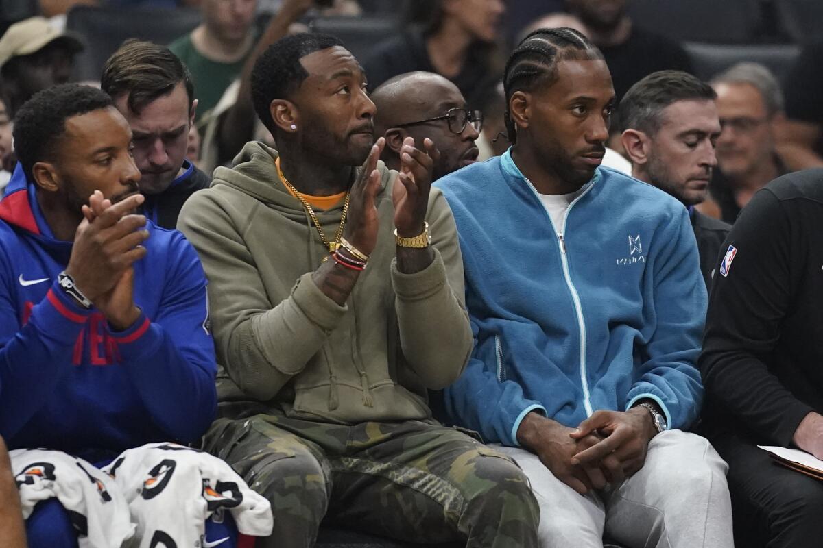 Clippers guard John Wall, center, and forward Kawhi Leonard, right, sit on the bench.