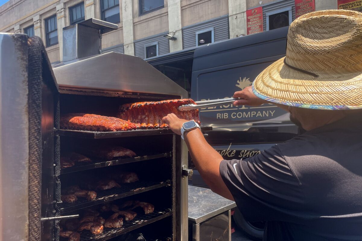 A person wearing a straw hat uses tongs to lift a rib off the grill 