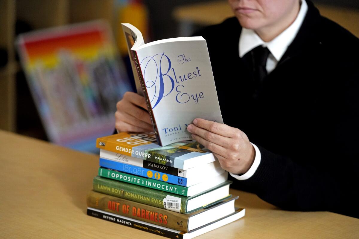 A person reading the book "The Bluest Eye," which is propped on a stack of books