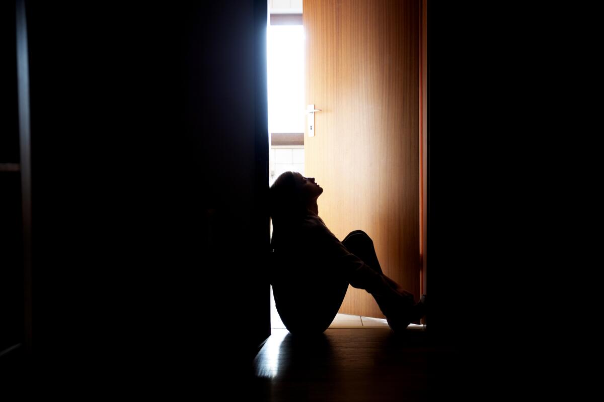 A backlit teenager sitting in a dark indoor doorway 