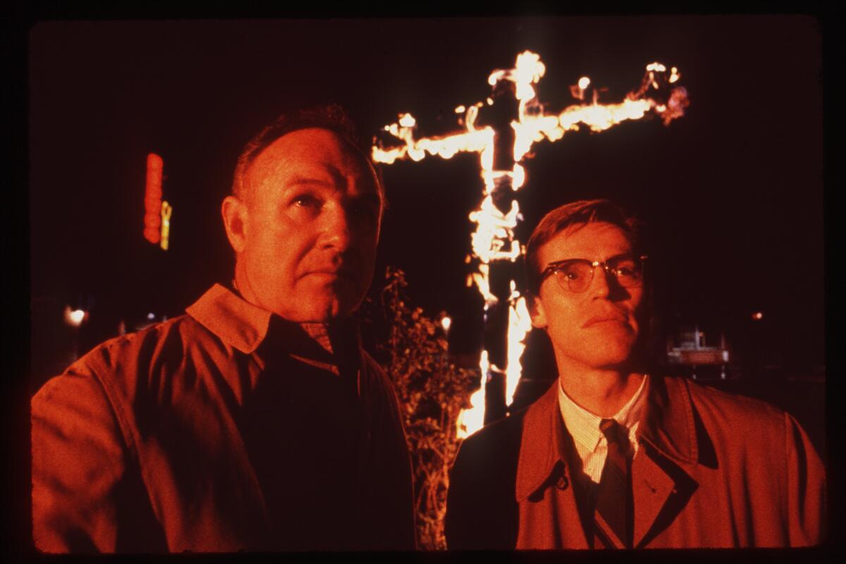 Two men standing in front of a burning cross.