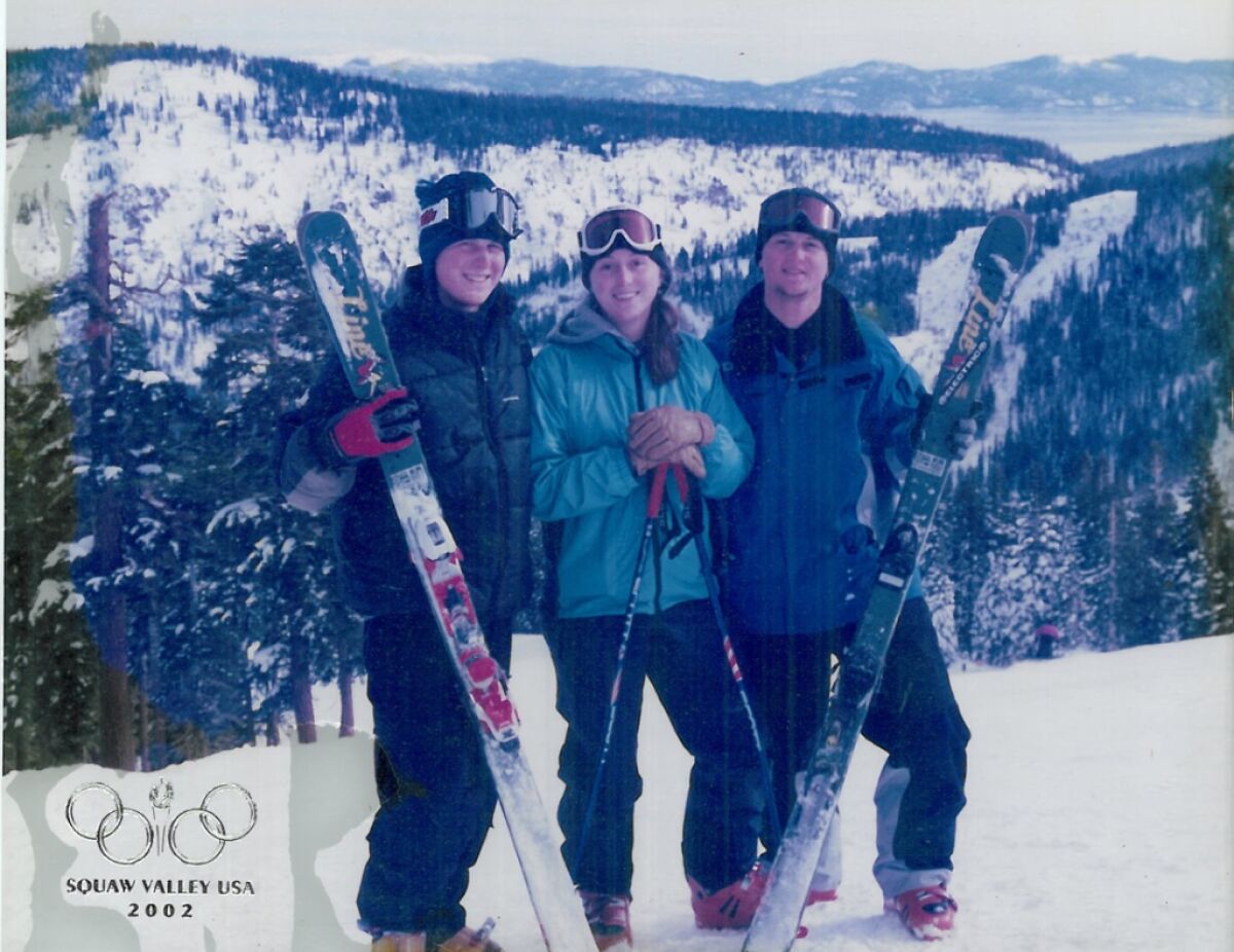 Three young people are smiling and holding skis.