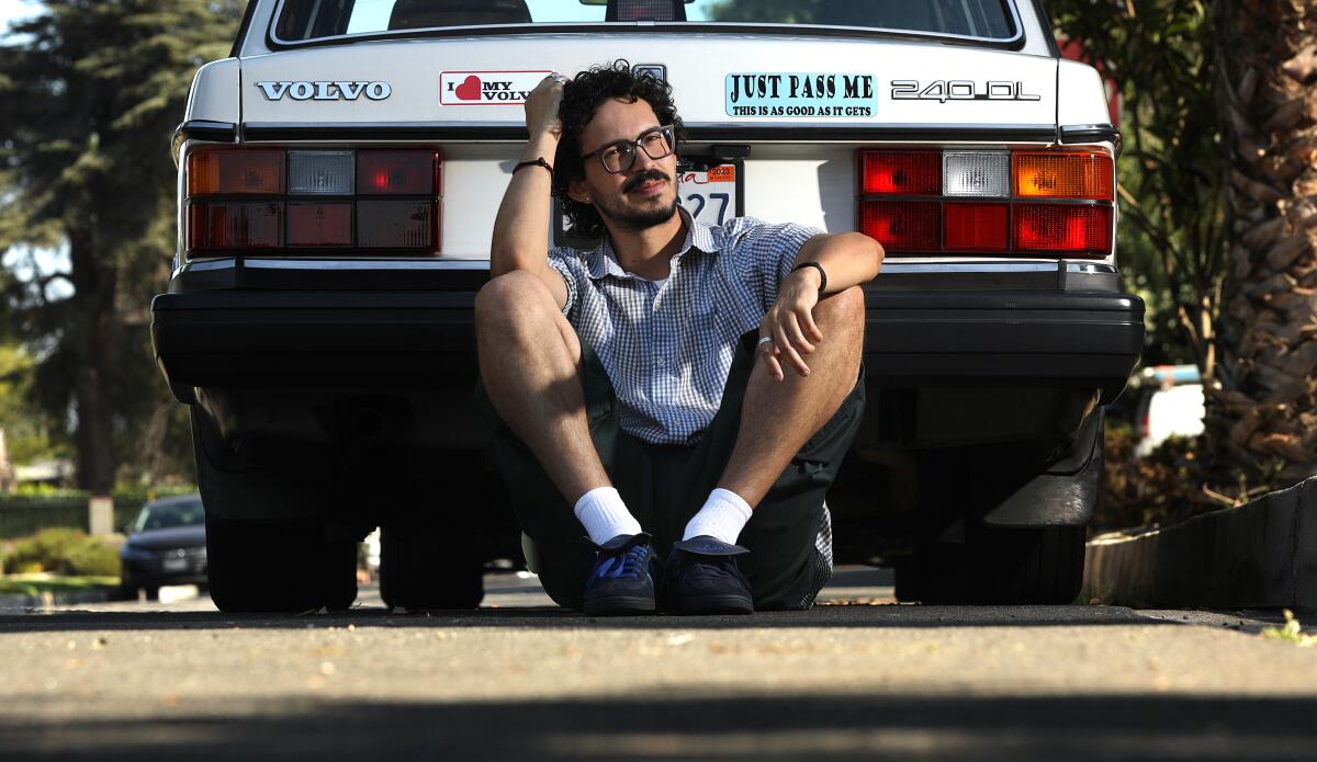 Vincent Enrique Hernandez sits on the ground, leaning against the back of his Volvo.