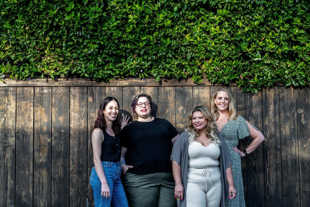 Four people stand in front of a wood fence.