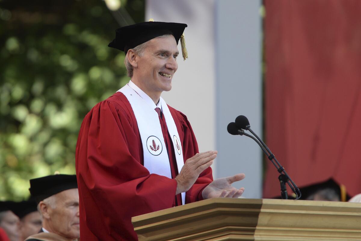 Stanford President Marc Tessier-Lavigne, wearing a red academic gown and mortarboard, speak at a lectern in 2016