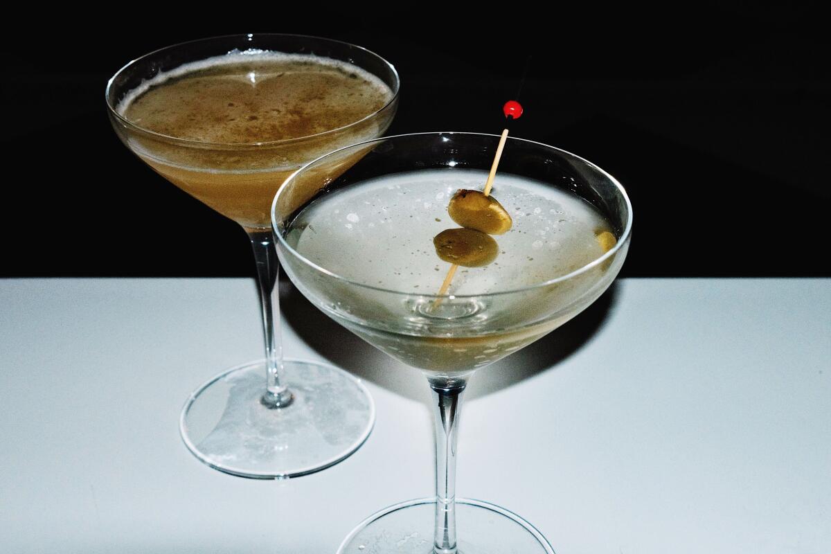 Two cocktails in coupe glasses, one garnished with olives