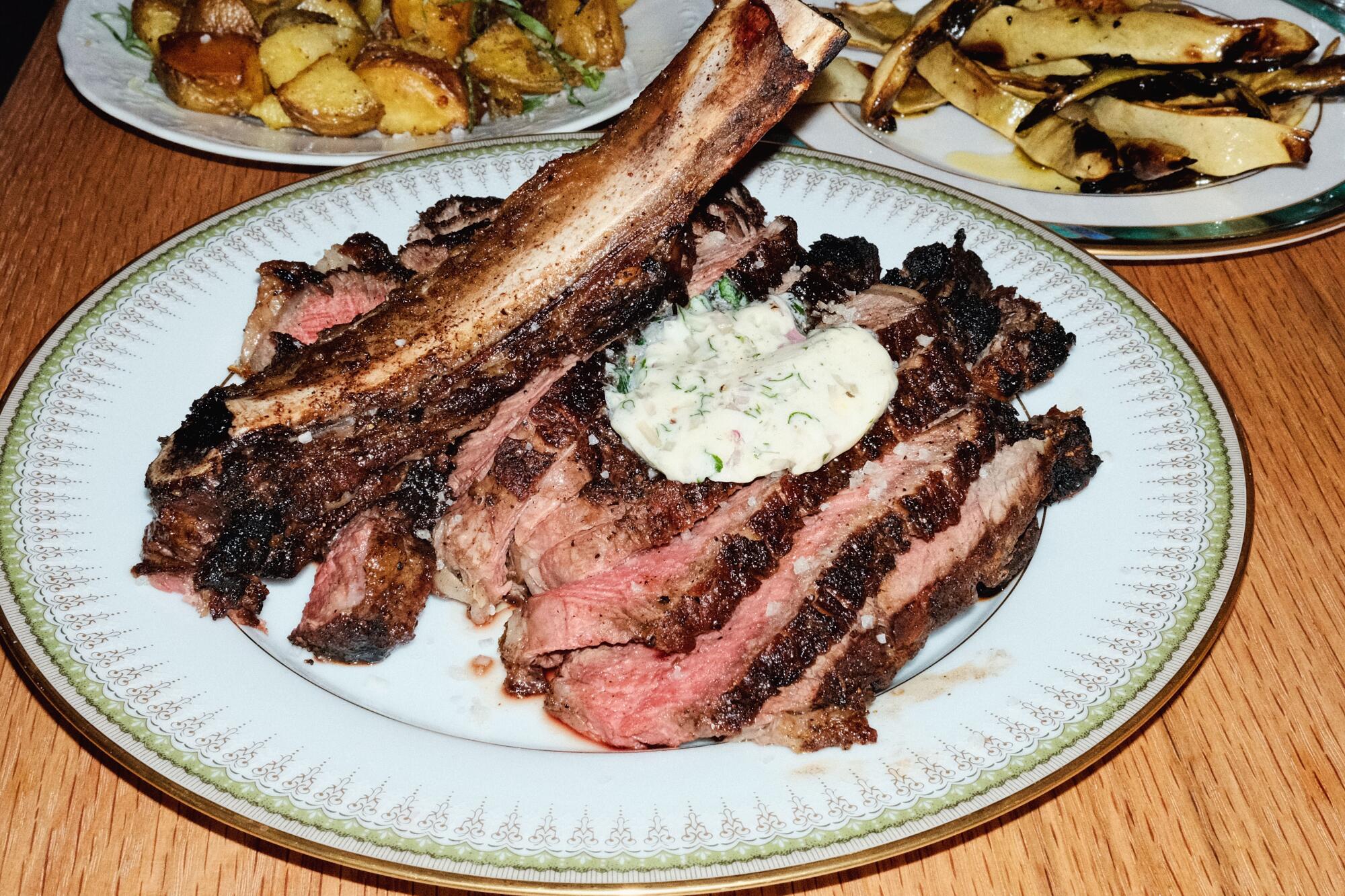 Costilla eye with bone with grilled Roman beans and roasted potatoes on a wooden table in Betsy in Altadena.