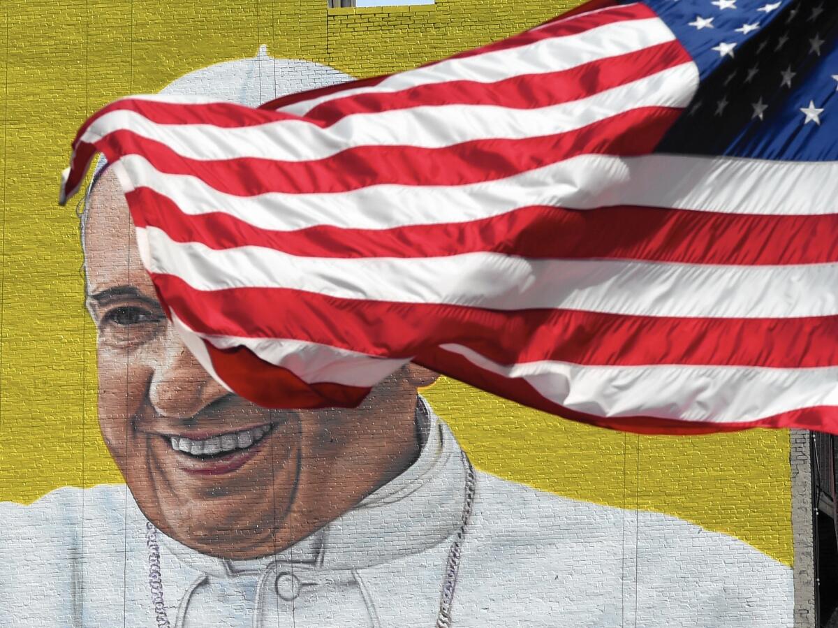 A U.S. flag blows in the wind in front of a mural of Pope Francis, located across the street from Madison Square Garden in New York City, on Sept. 21. The city is preparing for the religious leader's visit this week.