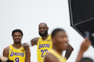 Bronny and LeBron James pose for photos at Lakers media day as Rui Hachimura takes a selfie in front of them.