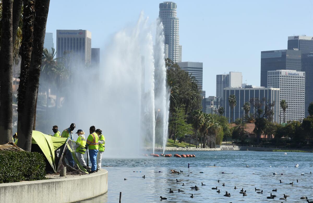 Work crews look over a tent next to Echo Park Lake, with the L.A. skyline in the background.