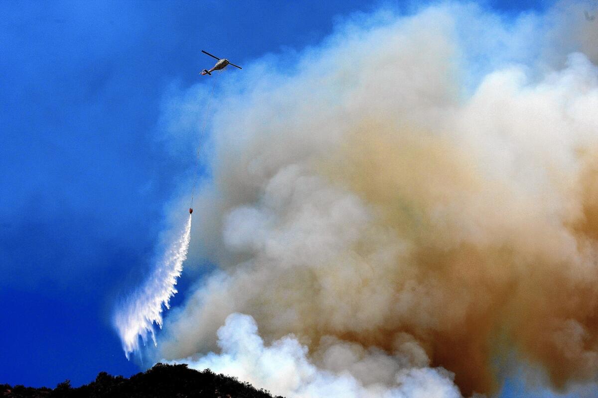 A helicopter makes a water drop on a brush fire near homes on Silverado Canyon Road as crews battle the Silverado fire in the Cleveland National Forest.