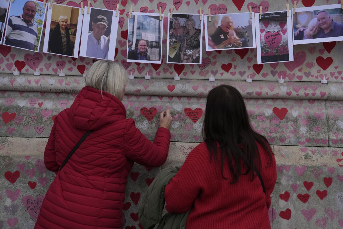 FILE - Family members write a message to two sisters who died of COVID on the National Covid Memorial wall in London, Tuesday, March 29, 2022. Latest figures from Britain's statistics agency show the prevalence of COVID-19 in the U.K. has reached record levels, with about 1 in 13 people estimated to be infected with the virus in the past week. Some 4.9 million people were estimated to have the virus in the week ending March 26, up from 4.3 million recorded in the previous week, the Office for National Statistics said Friday, April 1, 2022. (AP Photo/Alastair Grant, File)