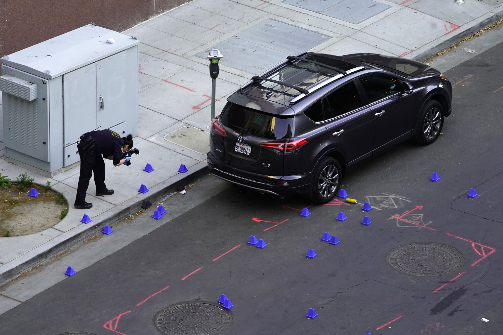 A person bends over to take photos of evidence markers scattered around a street and sidewalk