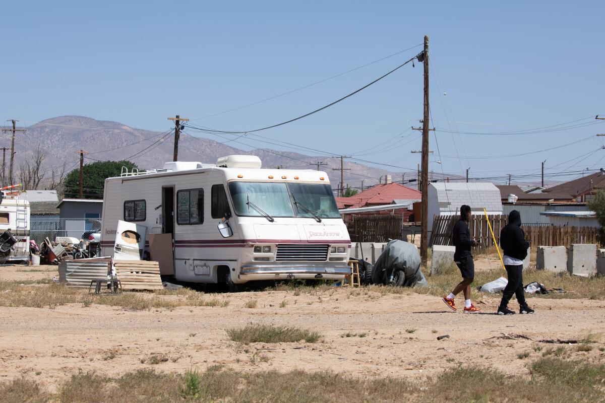 Two figures walking through a landscape of motor homes and houses, with arid mountains on the horizon. 