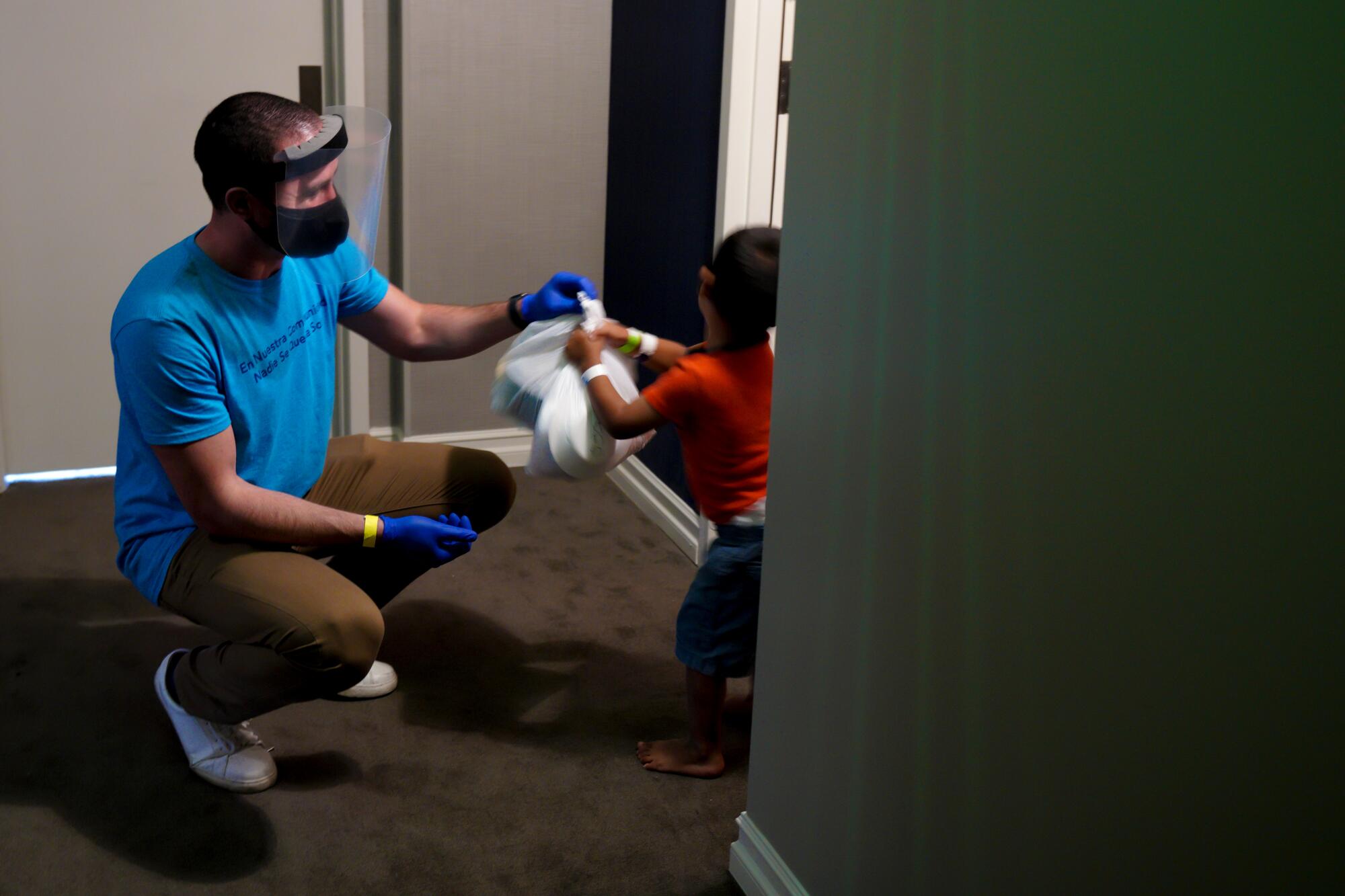 A man kneels and hands a young child a bag of food in a doorway