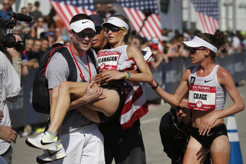 Steve Edwards carries his wife, Shalane Flanagan, after she fell to the ground in exhaustion following her third-place finish in the U.S. Olympic women's marathon trial on Saturday. Training partner Amy Cragg, who won the race, was the first to arrive at her side as Flanagan crossed the finish line.
