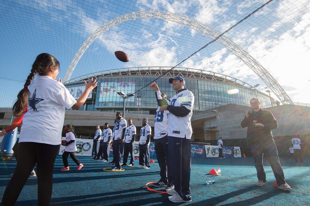 Cowboys quarterback Tony Romo tosses a football to a child during a community day event Tuesday outside of Wembley Stadium in London. Dallas plays the Jaguars on Sunday in England as part of the International Series.