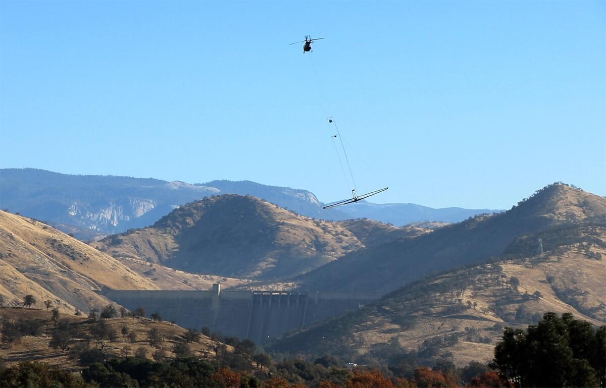 A helicopter flies near Pine Flat Dam towing an airborne electromagnetic system