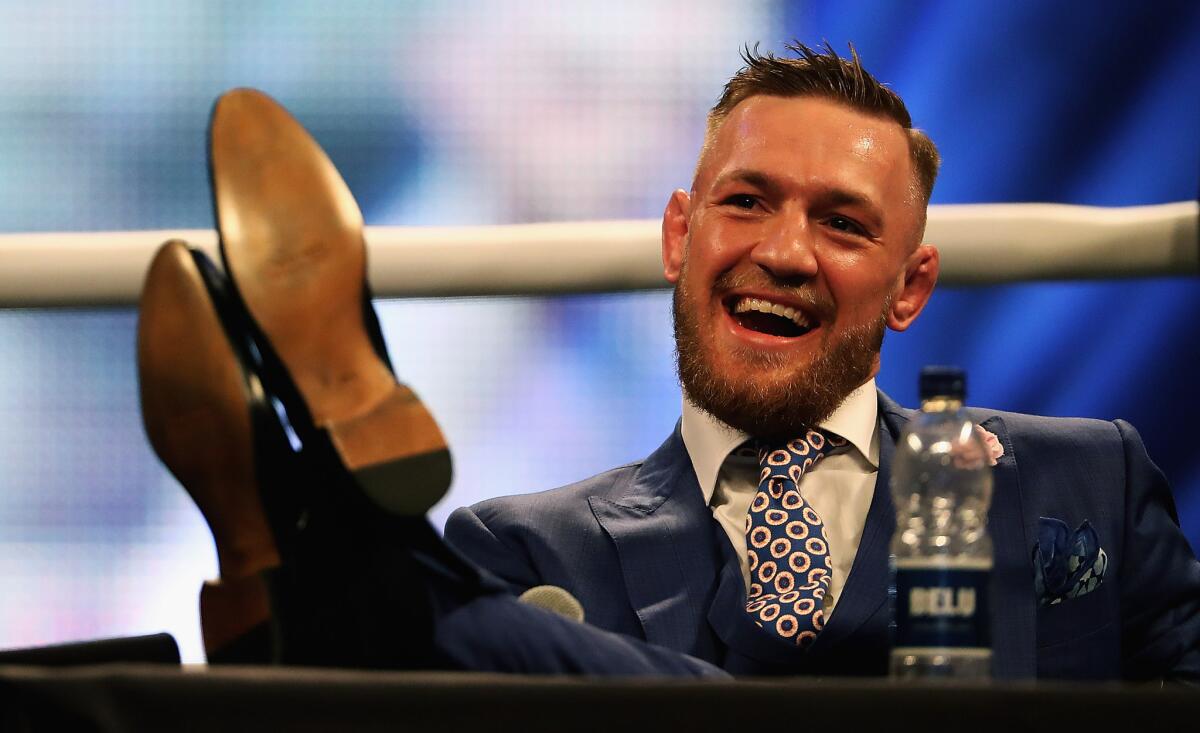 Conor McGregor chuckles while listening to Floyd Mayweather Jr. at their promotional stop in London on July 14.