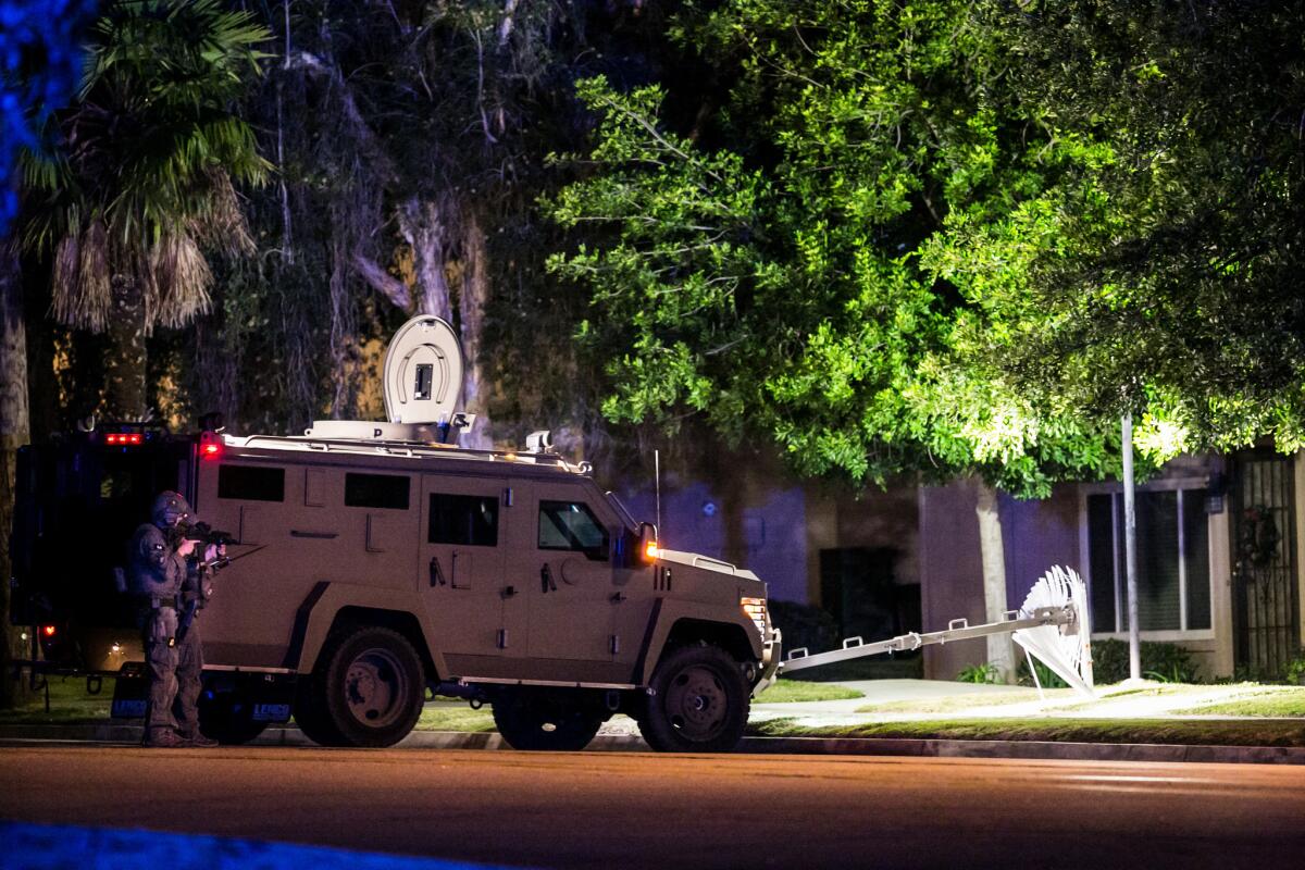 A SWAT team stands guard with a rifle pointed at a home that is being investigated by police after today's San Bernardino's mass shootings.